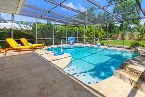 A covered swimming pool with a sunshade, lounge chairs, and a stone deck. - Pool Games More Fun for Everyone (Palm Harbor)