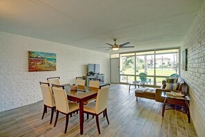 Un coin repas avec une table et des chaises en bois, un téléviseur posé sur un meuble, et une grande fenêtre donnant sur l’extérieur.