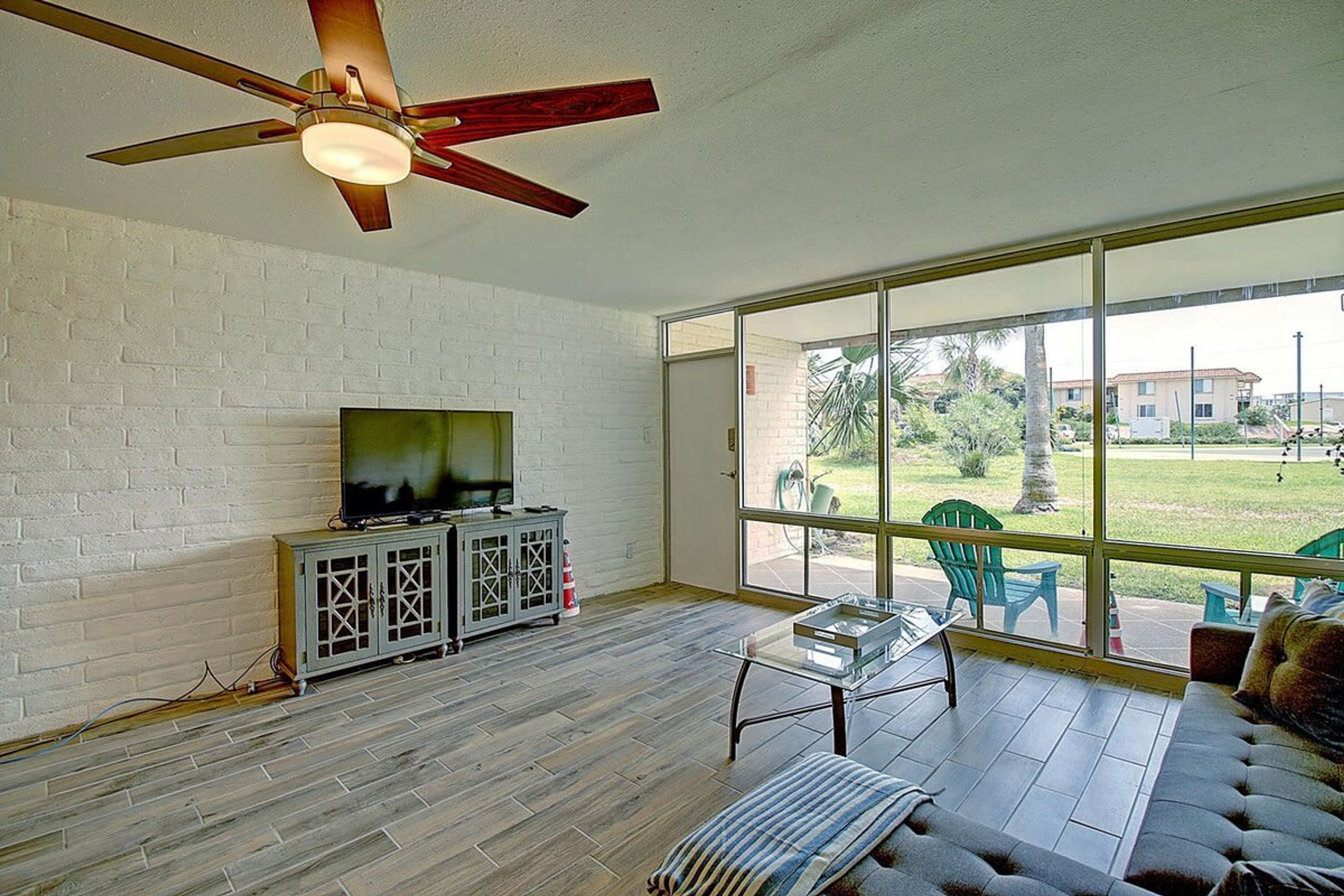 A spacious room with a television on a cabinet, a sofa, and a large window offering a view of the outdoors.