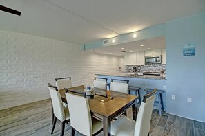 A dining area with a wooden table and chairs, a kitchen in the background, and a sign on the wall. - A Salty Day Getaway Beach Boardwalk Large Pool (Port Aransas)