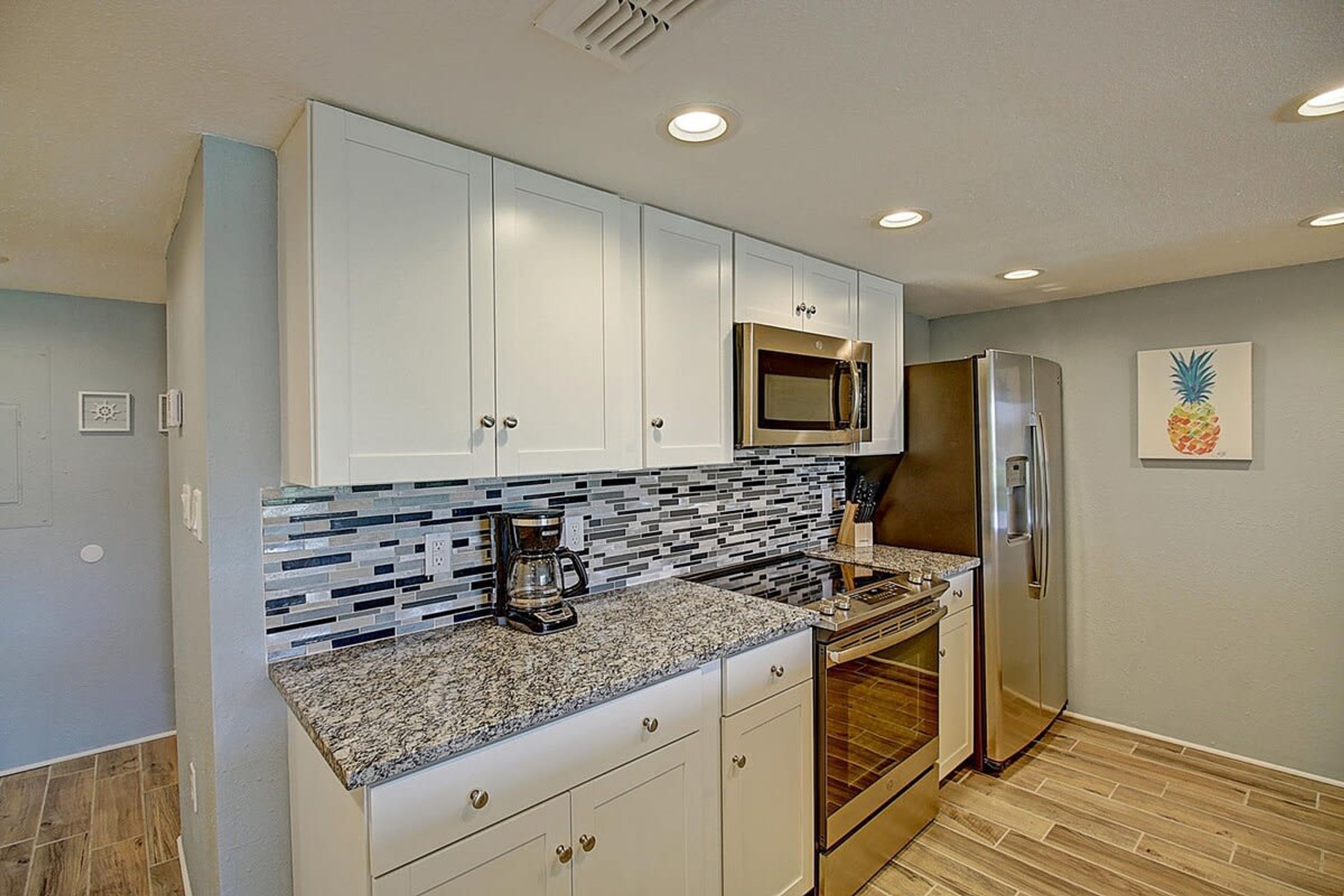 A kitchen with white cabinets, a stainless steel microwave, a refrigerator, and a coffee maker.