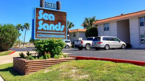 A sign for Sea Sands Condominiums with a clear view of the parking lot and a building with a red roof. - A Salty Day Getaway Beach Boardwalk Large Pool (Port Aransas)