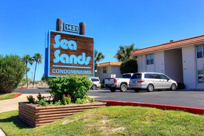 A sign for Sea Sands Condominiums with a clear view of the parking lot and a building with a red roof. - A Salty Day Getaway Beach Boardwalk Large Pool (Port Aransas)