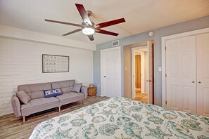 A bedroom with a bed, a ceiling fan, a wall with motivational quotes, a sofa, and a door leading to another room. - A Salty Day Getaway Beach Boardwalk Large Pool (Port Aransas)