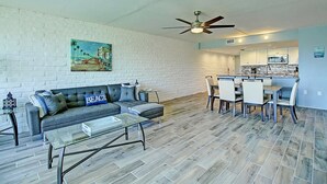 A living room with a sofa, coffee table, and a painting on the wall. - A Salty Day Getaway Beach Boardwalk Large Pool (Port Aransas)