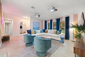 Ein modernes Wohnzimmer mit einer Eckcouch, zwei Zierteilen, einem Couchtisch, einer Stehlampe und einem großen Fenster mit Vorhängen.