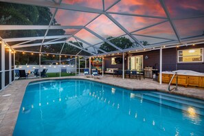 Ein Swimmingpool mit überdachtem Patio, Liegestühlen und einem Grill.