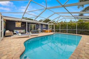 Ein Schwimmbad mit Glasveranda, Liegestühlen und Grillplatz.