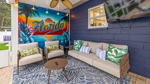 Una habitación con ventilador de techo, un mural grande con la palabra 'Florida', un conjunto de sofás y una mesita.