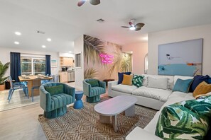 A modern living room with a sofa, chairs, a coffee table, and a dining area with a table and chairs. - Epic Indoor Slide Pool Hot Tub Mini Golf Fire Pit (Madeira Beach)