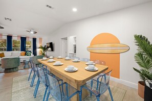 A modern dining area with a wooden table set for six, surrounded by blue chairs. - Epic Indoor Slide Pool Hot Tub Mini Golf Fire Pit (Madeira Beach)