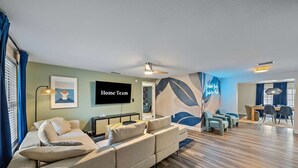 Ein modernes Wohnzimmer mit einem großen Flachbildfernseher, einem Ecksofa und einem Essbereich mit Tisch und Stühlen.