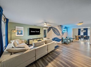 A modern living room with a large flat-screen TV, a sectional sofa, and a dining area with a table and chairs. - Pool Hot Tub Game Room More - Sleeps 10 (Bradenton)