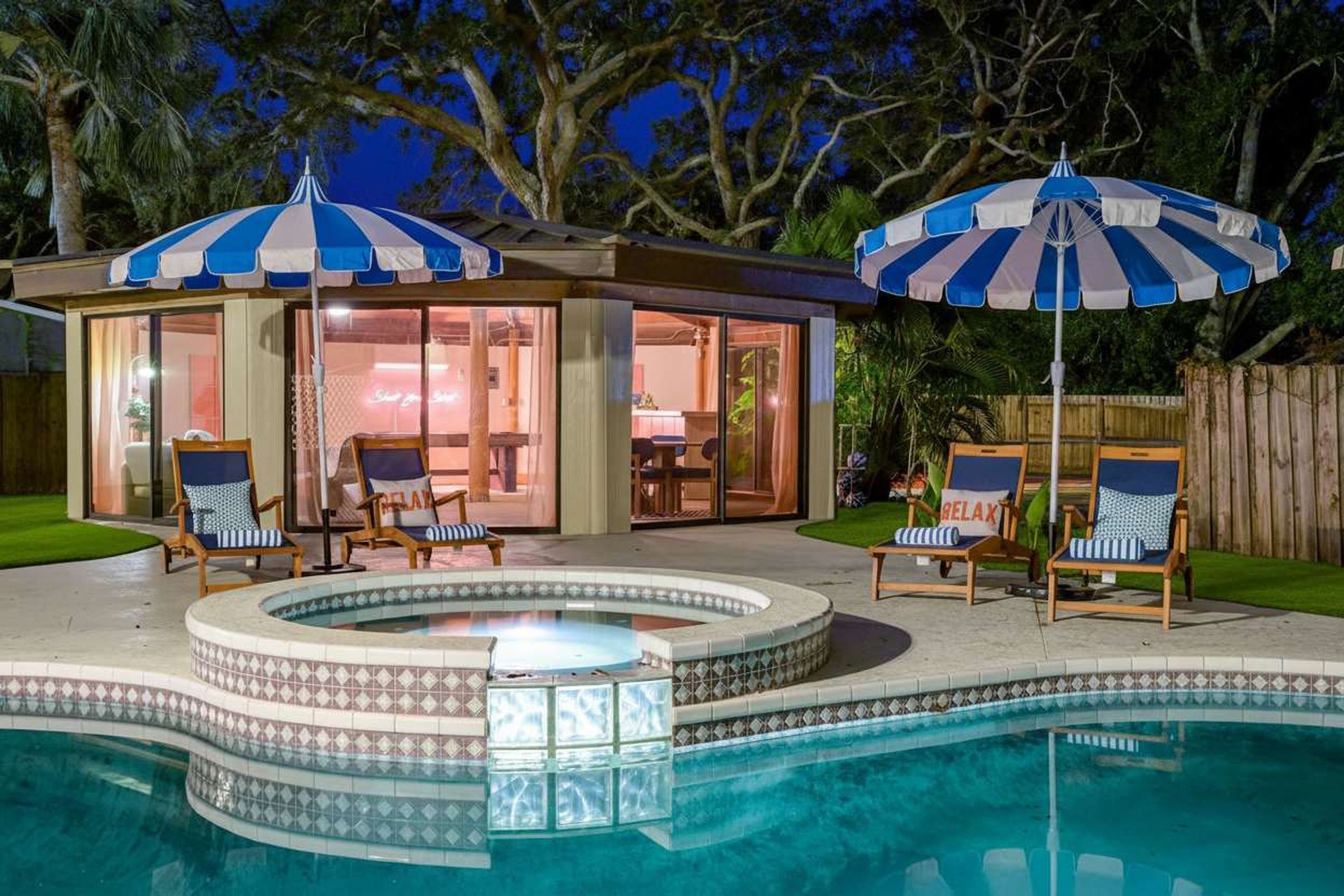 A poolside area with a hot tub, lounge chairs, and umbrellas.