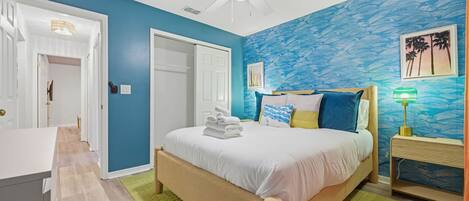 Un dormitorio con cama, mesita de noche, ventilador de techo y pared con diseño azul.