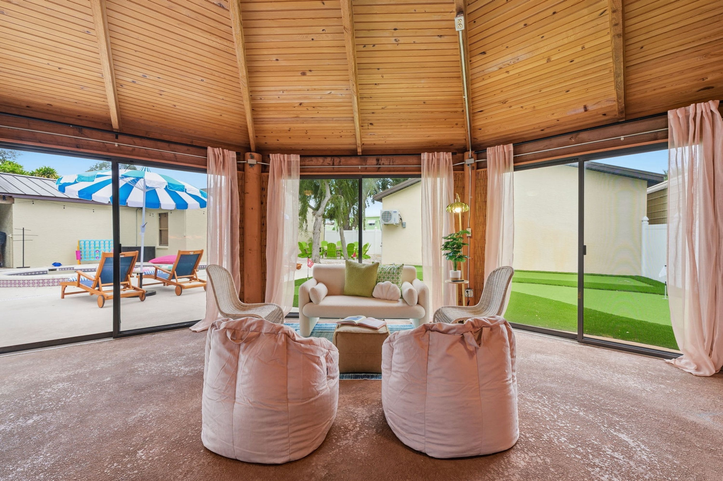 A spacious room with a high ceiling, a large sliding glass door leading to an outdoor area with a pool and lounge chairs.