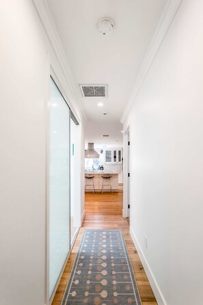 Um corredor com tapete estampado que leva a uma cozinha com piso de madeira e armários brancos.