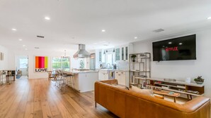 Una cocina moderna con una isla central, un comedor con un taburete de bar y una sala de estar con un televisor grande.