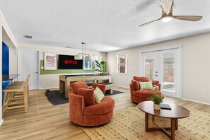 Ein modernes Wohnzimmer mit Flachbildfernseher, zwei Sesseln, einem Couchtisch und einem Deckenventilator.