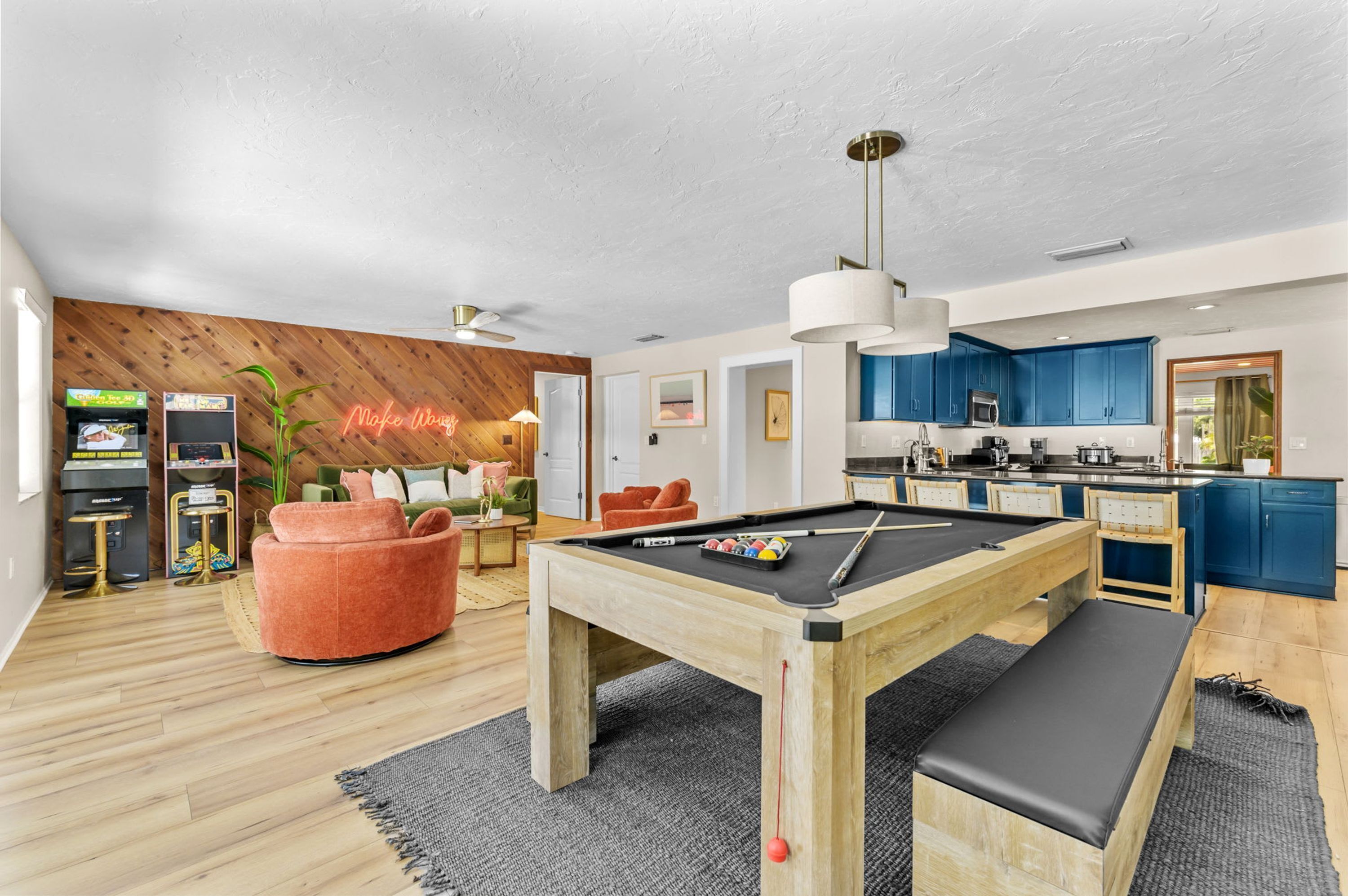 A modern living space with a pool table, a neon sign, a kitchen, and a wooden wall.
