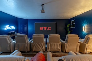 Ein Heimkino mit einer großen Leinwand, die 'NETFLIX' zeigt, und mehreren Relaxsesseln.