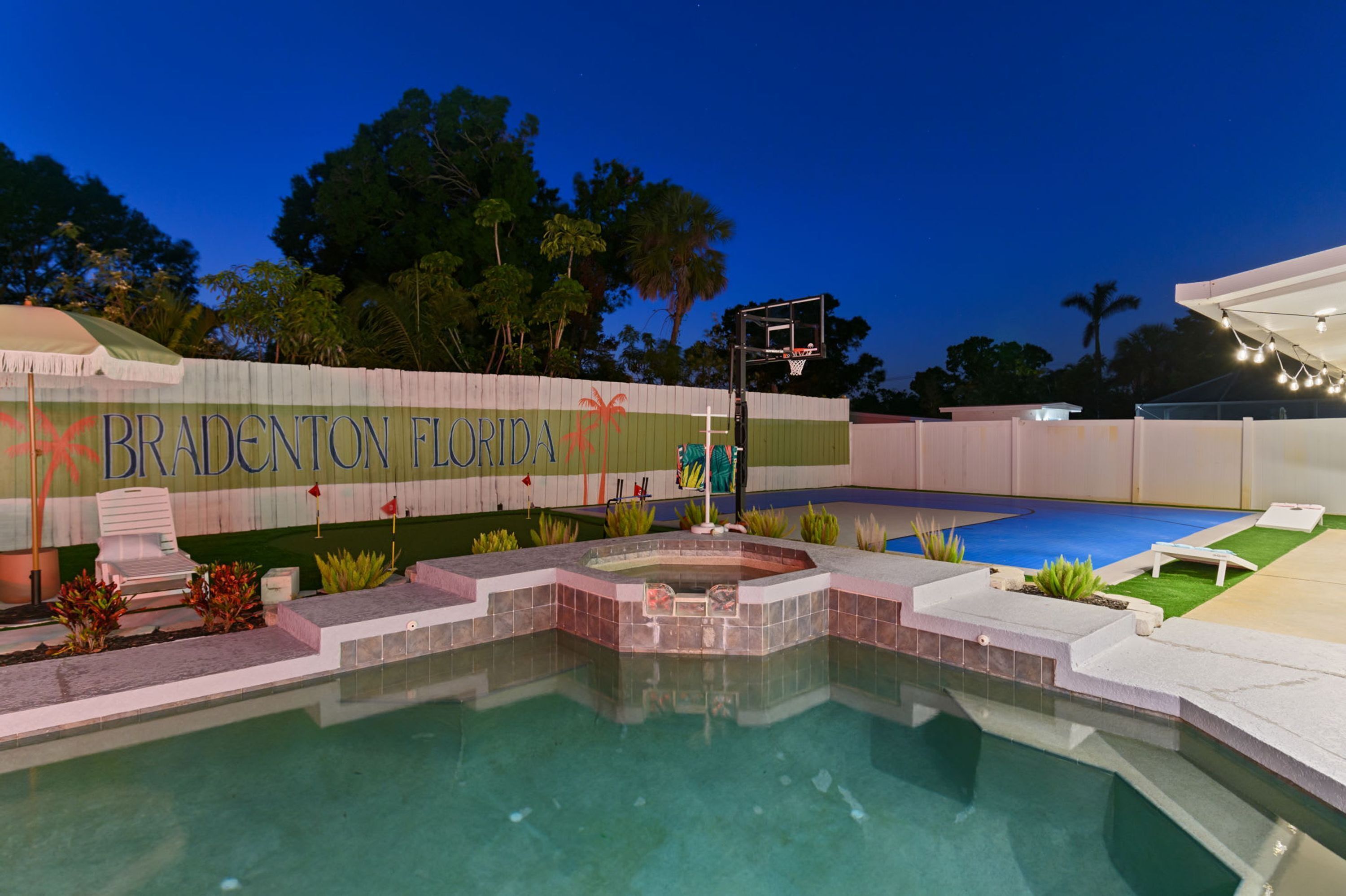 Une piscine avec un panier de basketball, entourée d’une clôture sur laquelle est affiché un panneau indiquant « BRADENTON, FLORIDE ».