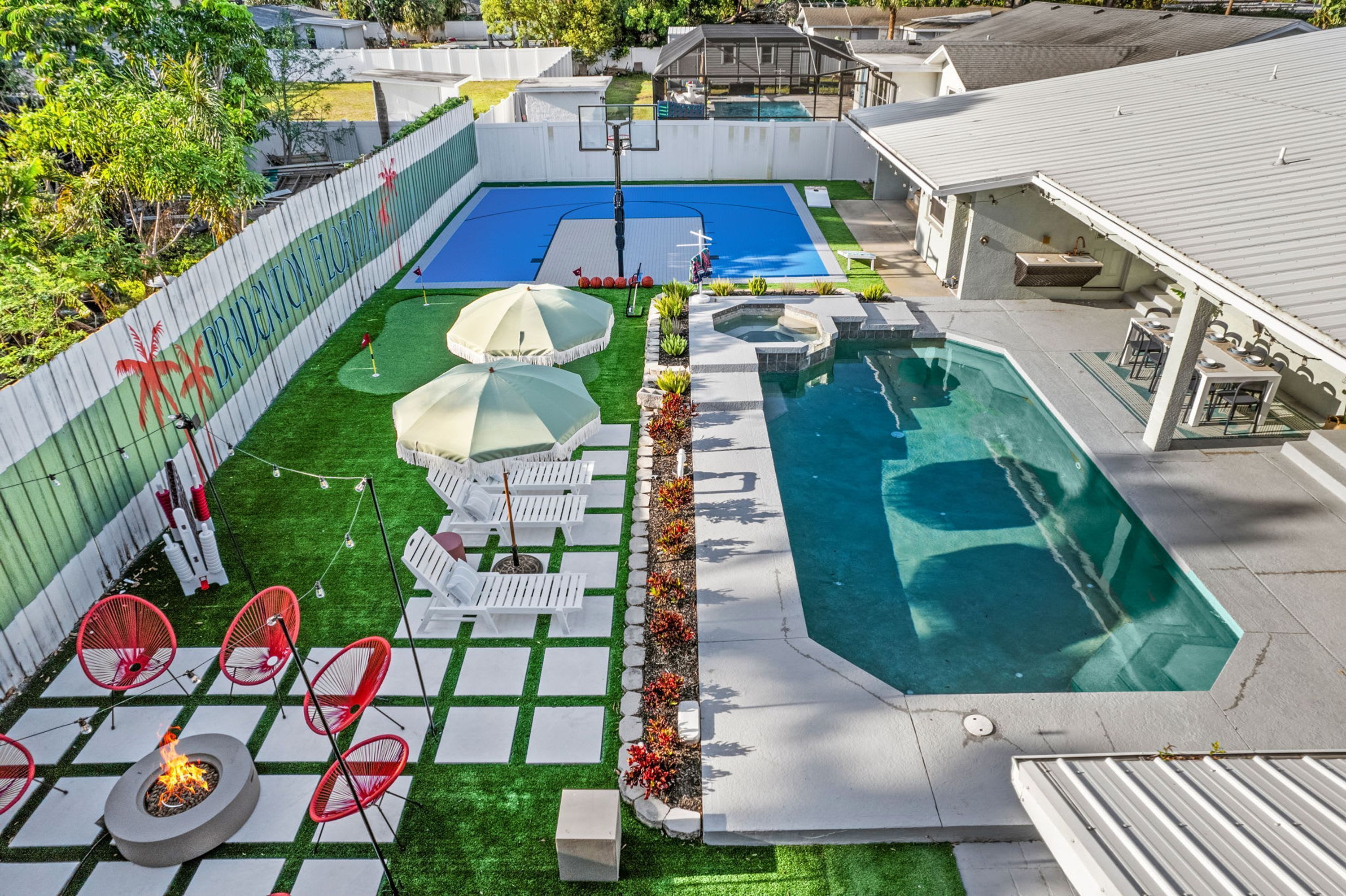 Un patio trasero con piscina, cancha de baloncesto y mobiliario de exterior.