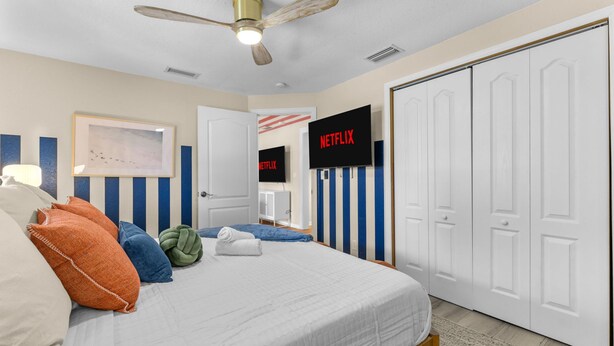 A bedroom with a bed, pillows, a ceiling fan, a framed picture, a television, and a wardrobe. - Sleeps 20 Basketball Court Pool Movie Room (Bradenton)