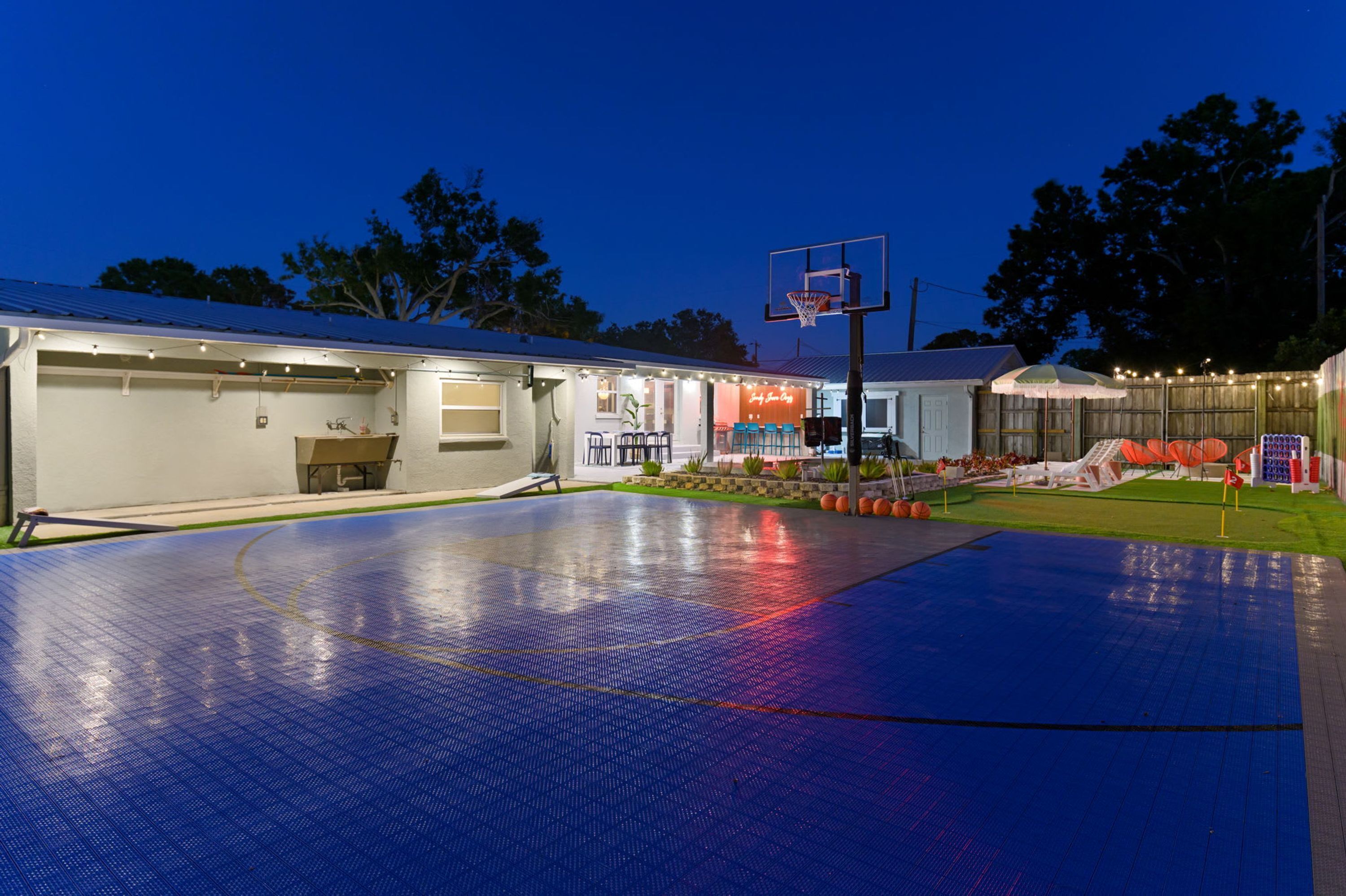 A basketball court with a hoop, a covered seating area, and a building with a garage.