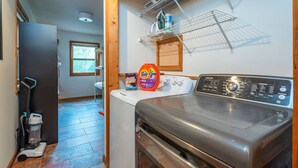 A laundry room with a front-loading washing machine, a drying rack, and a shelf with cleaning supplies. - Sleeps 20 Hot Tub Outdoor Theater Fire Pit Games (Fairview)