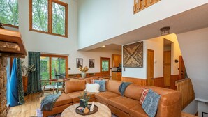 A spacious living room with a large sectional sofa, a round ottoman, and a dining area with a table and chairs. - Sleeps 20 Hot Tub Outdoor Theater Fire Pit Games (Fairview)