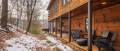 Una cabaña de madera con un porche cubierto, mobiliario exterior y vistas a un paisaje nevado.