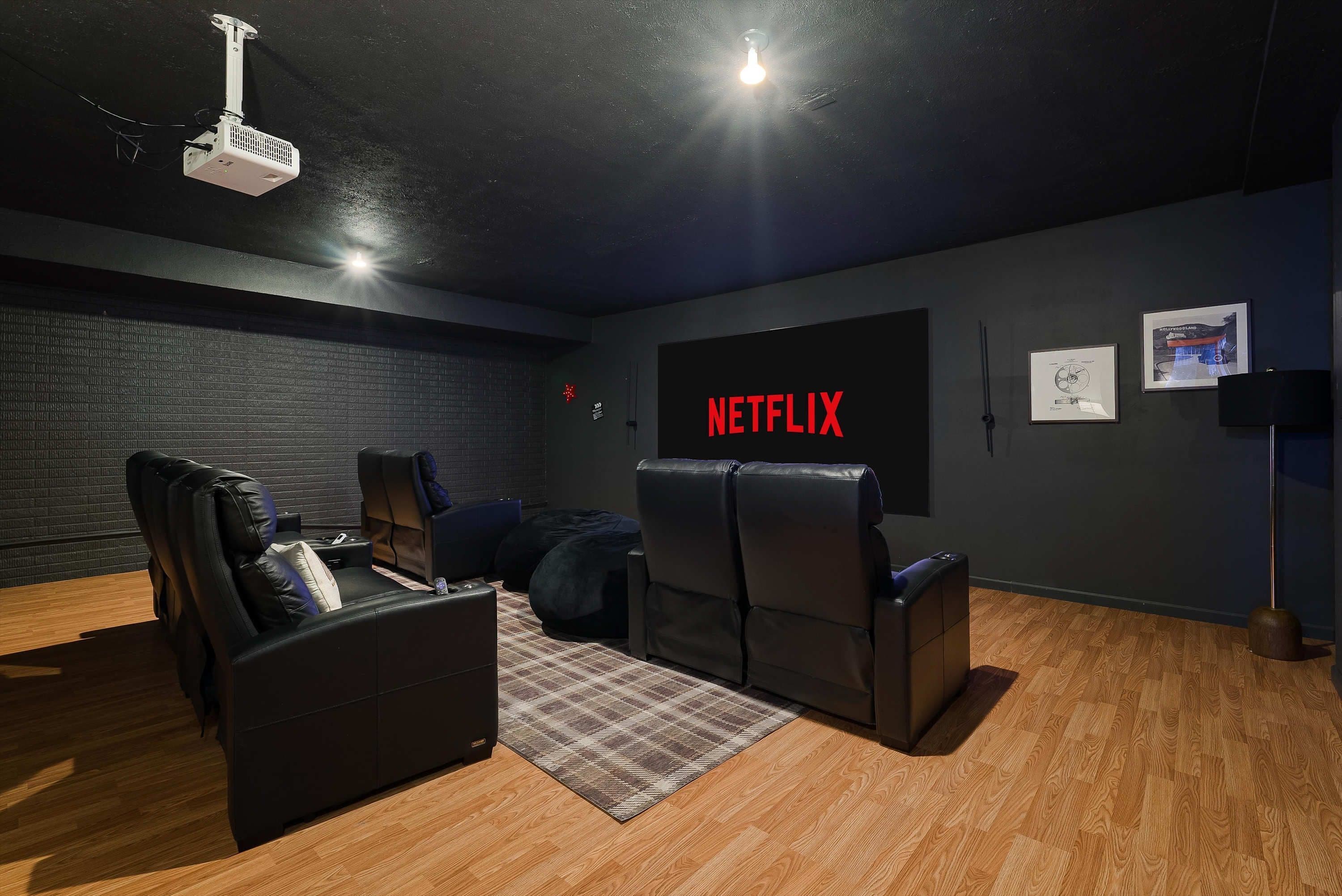 A home theater room with a large flat-screen TV displaying 'NETFLIX', a projector, and comfortable seating.