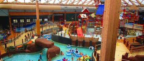 Parque acuático interior con varias piscinas, toboganes y zonas de juego.