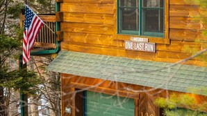 Una cabaña de madera con una puerta verde, un cartel que dice 'ONE LAST RUN' y una bandera estadounidense.