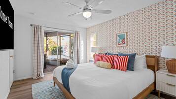 A hotel room with a bed, a ceiling fan, a window with curtains, a wall with a patterned wallpaper, and a small framed picture.