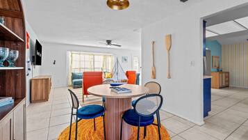 A dining area with a round table, two blue chairs, a wooden sideboard, and a ceiling fan.