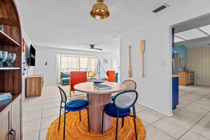 Uma sala de jantar com mesa redonda, duas cadeiras azuis, um aparador de madeira e um ventilador de teto.