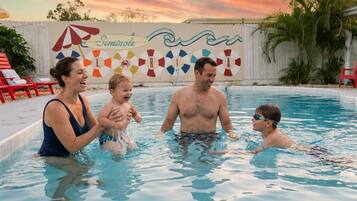 Una piscina con un atardecer de fondo, un puesto de salvavidas y una valla con palmeras.