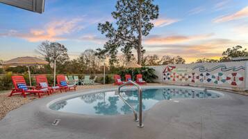 A pool area with lounge chairs and umbrellas, surrounded by trees and a decorative wall.