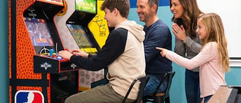 Una familia jugando a una máquina recreativa de NBA JAM.