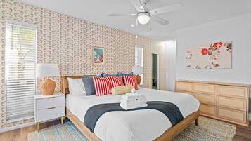 A bedroom with a bed, bedside tables, a dresser, a ceiling fan, and patterned wallpaper.