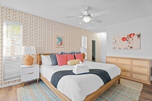 Un dormitorio con cama, mesitas de noche, cómoda, ventilador de techo y papel tapiz estampado.