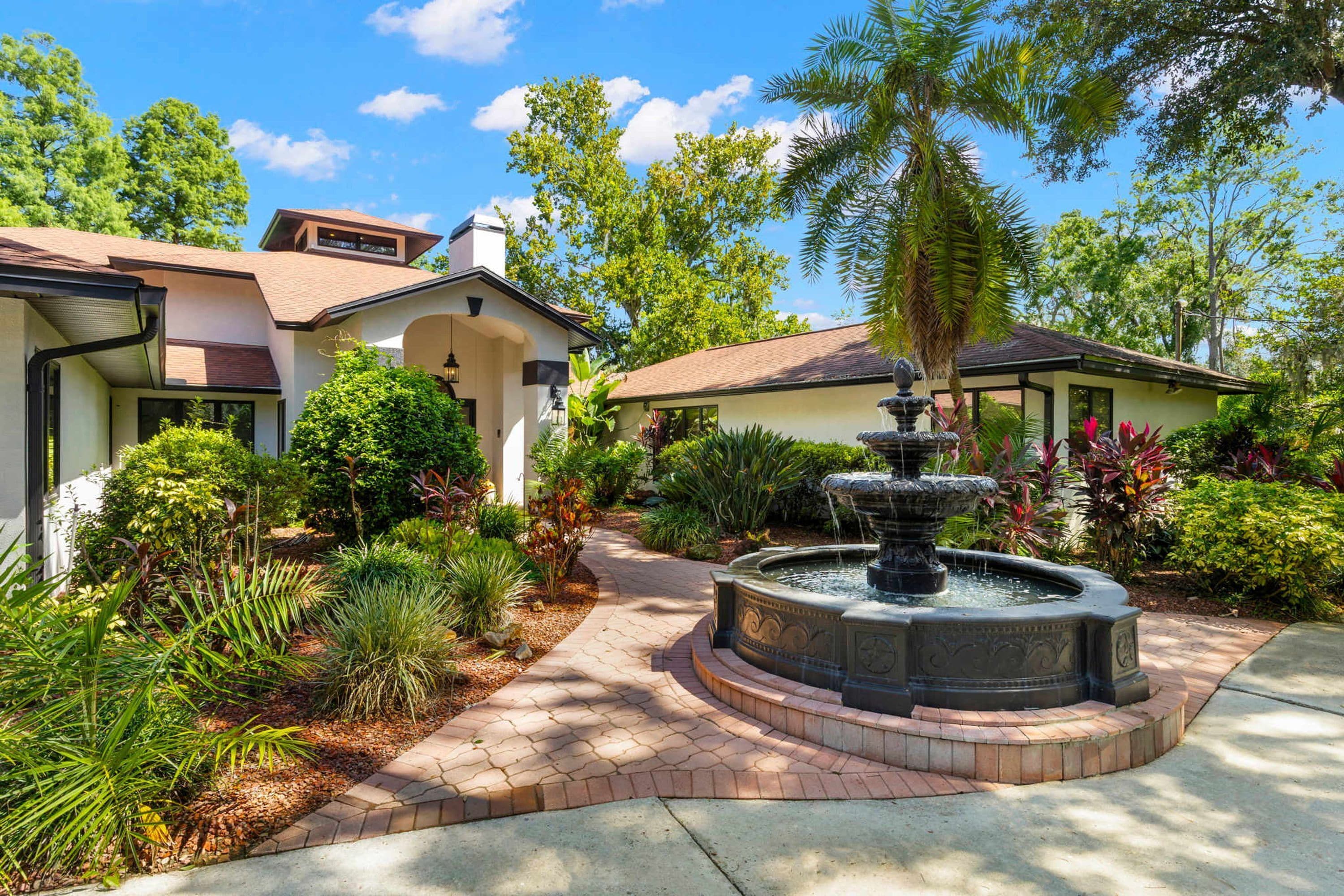 A residential property with a landscaped garden, a fountain, and a pathway leading to a house with a tiled roof.