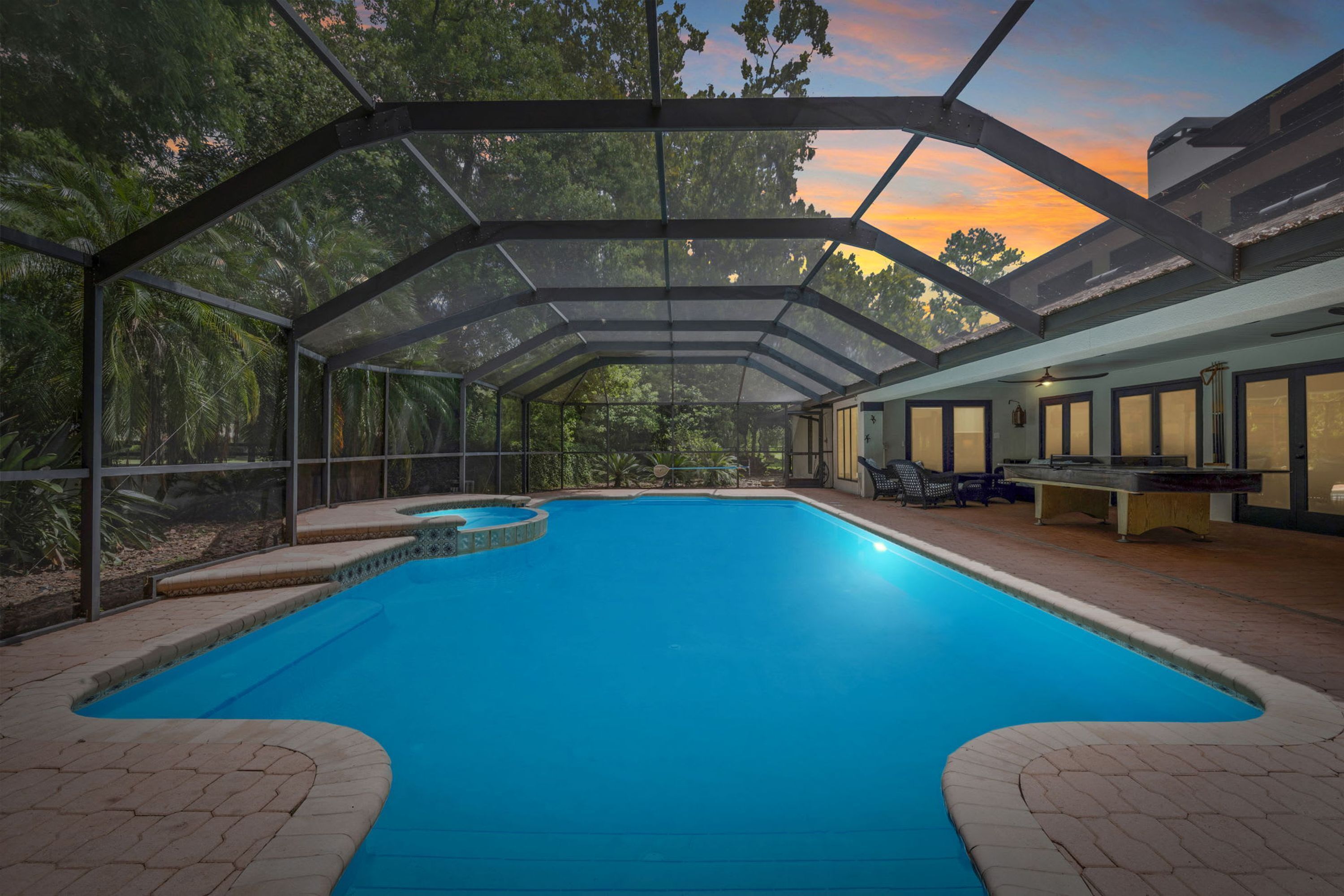 Une piscine couverte avec vue sur les arbres et un coucher de soleil.