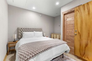A bedroom with a tufted headboard, a white bedspread, a fluffy throw blanket, a wooden wardrobe, and a nightstand with a lamp. - Tampa Oasis Private Pool Sauna Sleeps 14 (Tampa)
