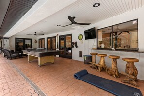 Une table de billard, un jeu de fléchettes et un coin bar avec des tabourets.