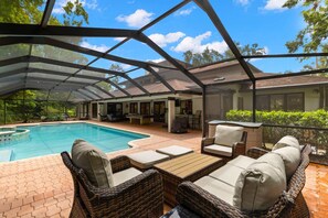 A covered outdoor swimming pool area with wicker furniture and a view of the surrounding landscape. - Tampa Oasis Private Pool Sauna Sleeps 14 (Tampa)