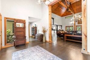 Un interior espacioso con techo alto, vigas de madera, alfombra grande y una zona de comedor con sofá de cuero.