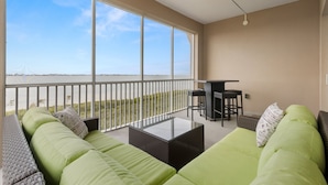 A balcony with a sofa, a table, and a bar area, overlooking a beach. - Bradenton Retreat-pool Stunning Views More (Bradenton)
